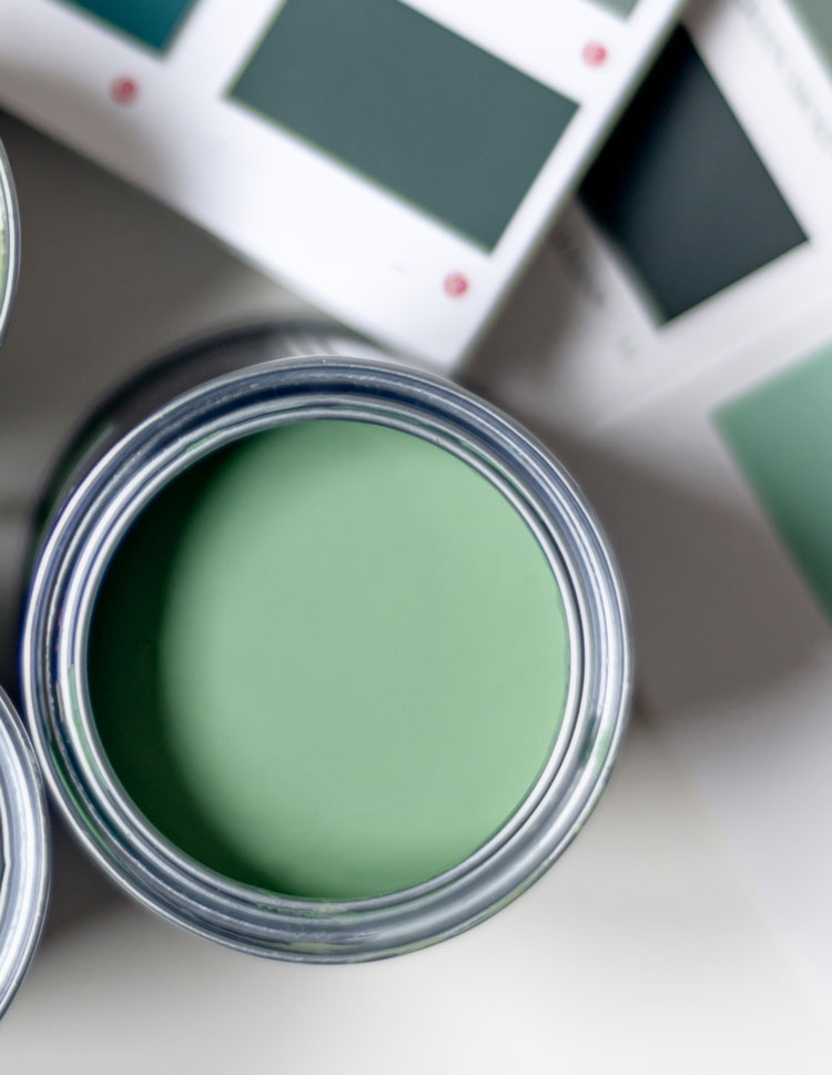 Focus on a light-green container of paint, with out-of-focus dark and light green paint swatches in the background.