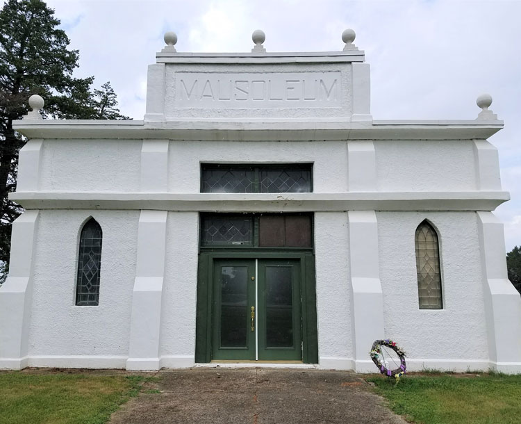 A Mausoleum in Zearing, painted white with a dark green door.