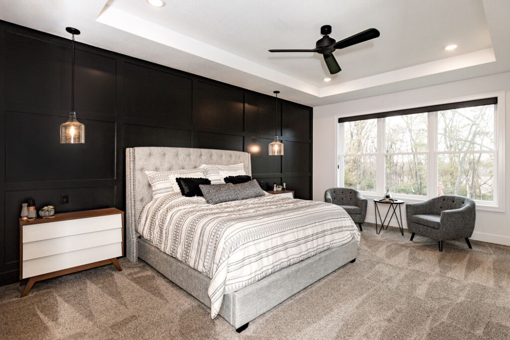 A bedroom with white walls and ceiling. The accent wall behind the bed has paneling and is painted black.